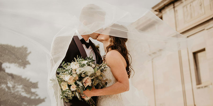a groom and a bride kissing while she's holding a bouquet of flowers